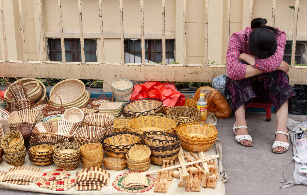 Woman sleeping next to baskets for sale on sidewalk