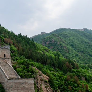 A stone wall runs up a steep hill with more green hills beyond