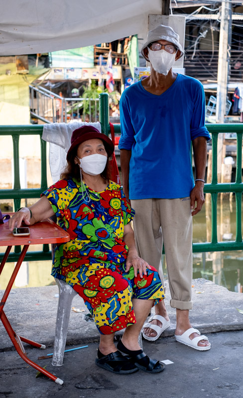 a woman sitting and a man standing along a railing next to a canal