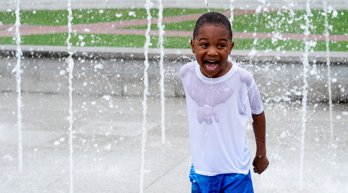 boy who has a huge smile while playing in a fountain