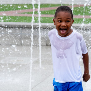 boy who has a huge smile while playing in a fountain