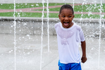 boy who has a huge smile while playing in a fountain