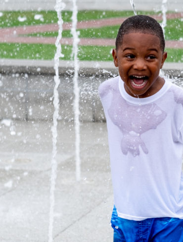 boy who has a huge smile while playing in a fountain