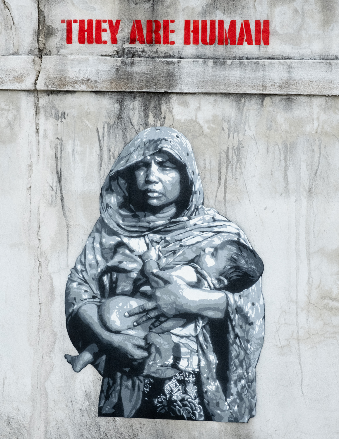 Gray and white graffiti image of a mother and child under the stencil "they are human"