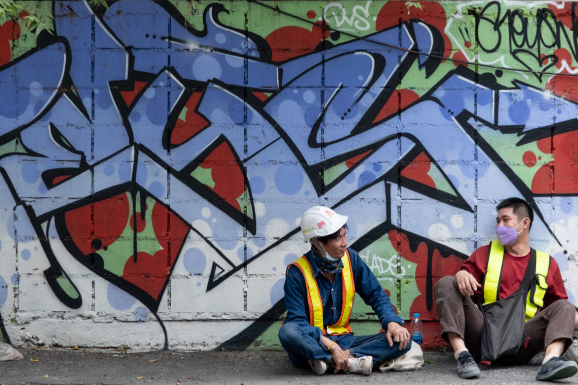 two workers on a break in front of of colorful graffiti of stylized writing