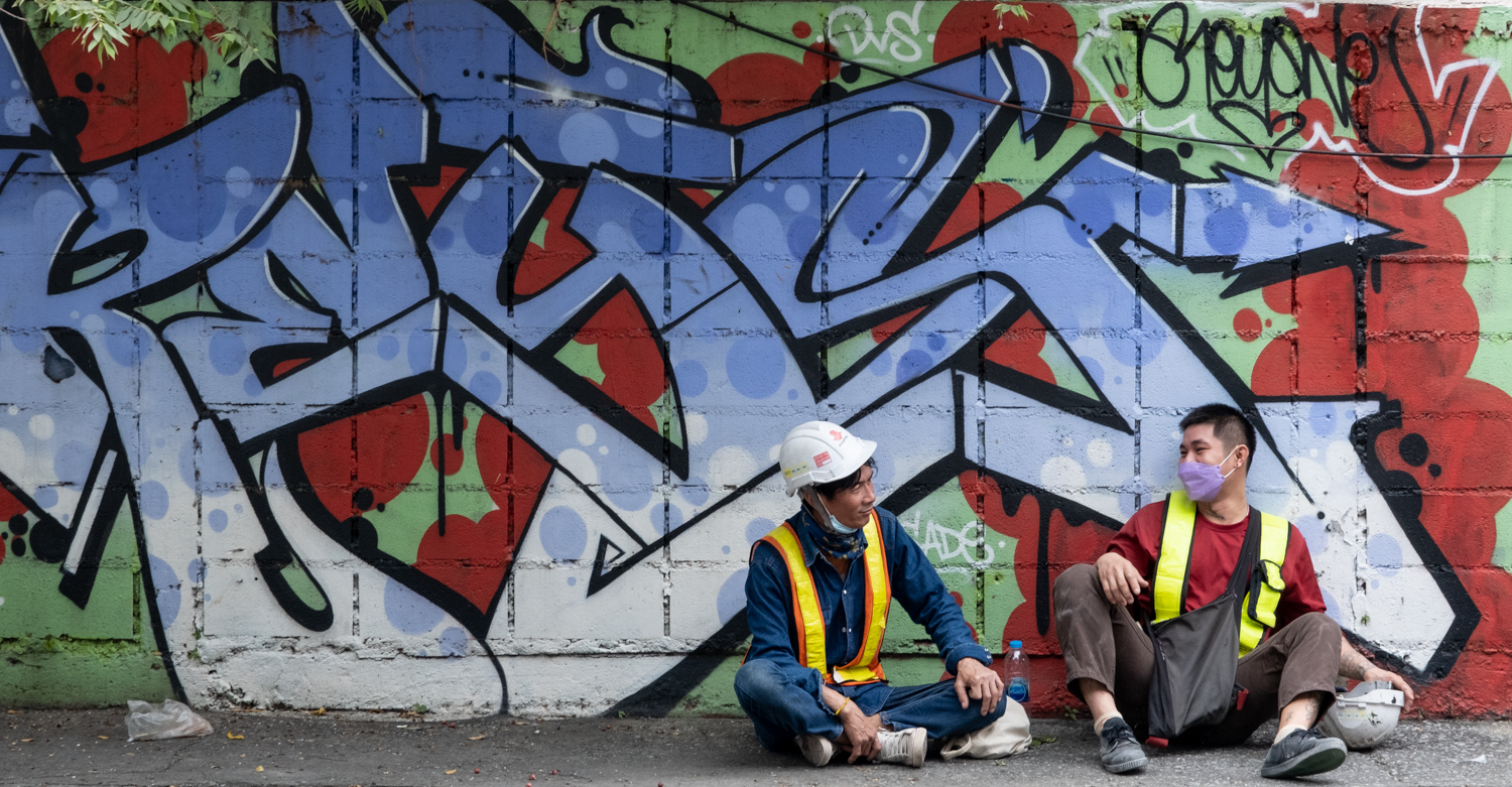 two workers on a break in front of of colorful graffiti of stylized writing