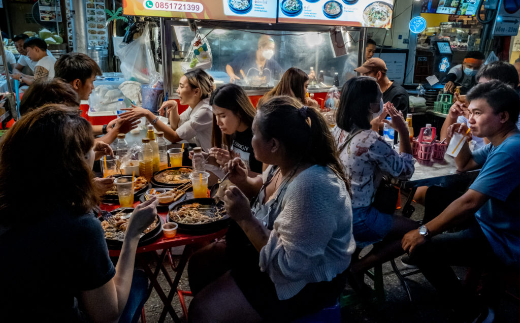 tables in the street with lots of diners eating food