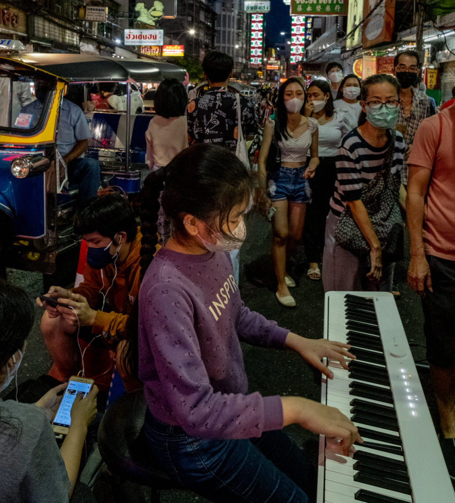 girl perhaps 10 years old plays electric piano on the busy sidewalk